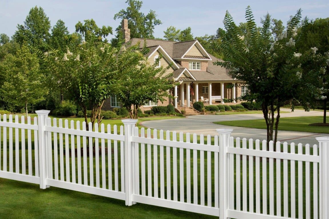 White vinyl picket fence in front of a house and lawn